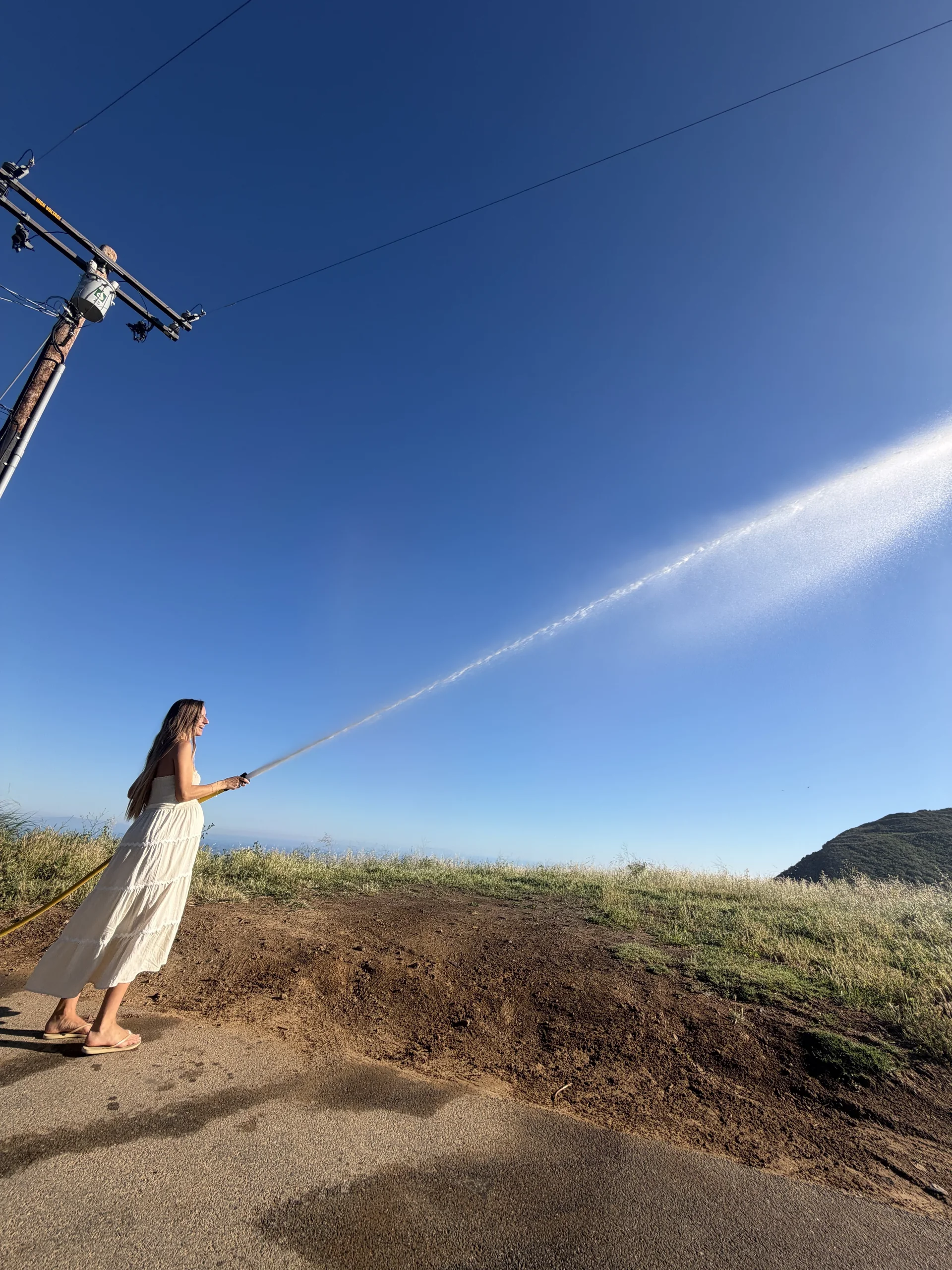 A pregnant woman easily operating a Hainy Hydrant with a powerful arc of water arcing across a Malibu hillside