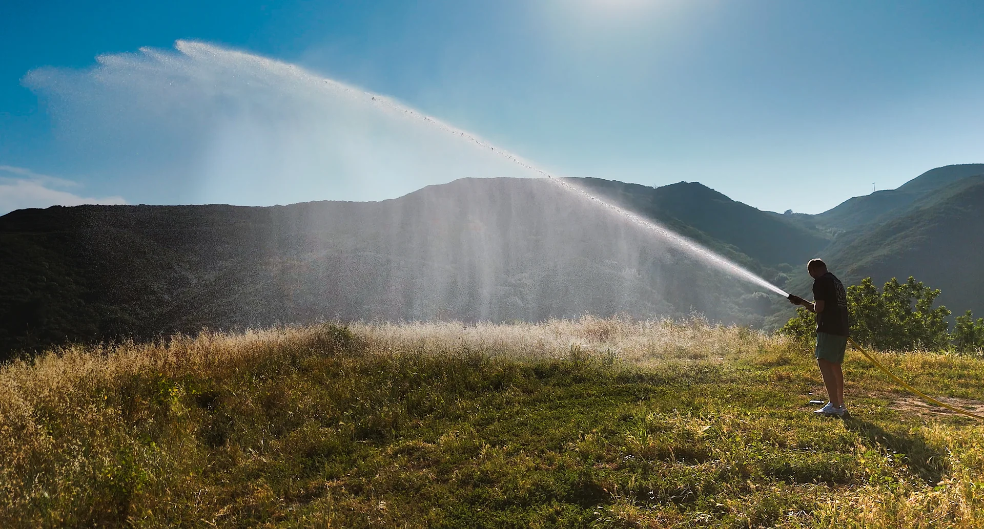 A person holding a Hainy Hydrant fire hose, water arcing high and far across the hillside